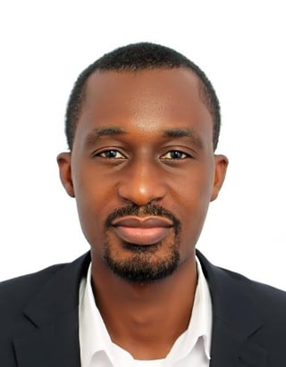 Professional headshot of a man with dark hair and beard wearing a black blazer and white shirt against a white background